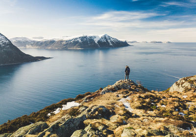 Rear view of person standing on rock by sea against sky