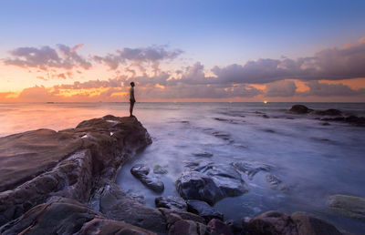 Full length of man standing on rock by sea against sky