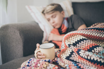 Boy sleeping while holding cup on sofa at home