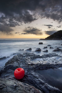 Red buoy on rocky shore against sky during sunset