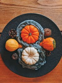 Background of autumn harvest of small orange different pumpkins on black plate close up. top view