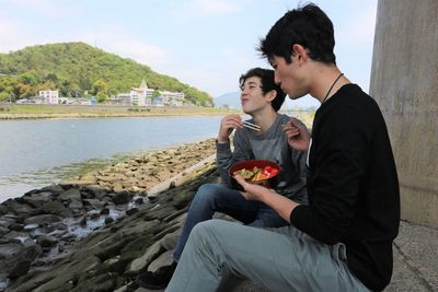 Young men sitting at riverside eating fruit