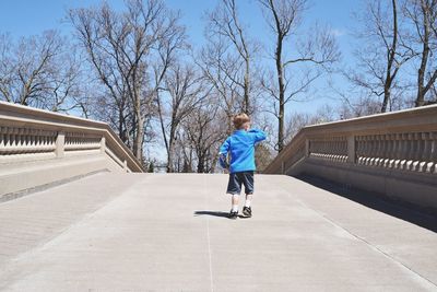 Rear view of boy walking on road against bare trees