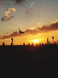 Silhouette of airplane flying against sky during sunset