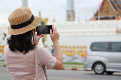 Midsection of woman photographing with mobile phone while standing on city street