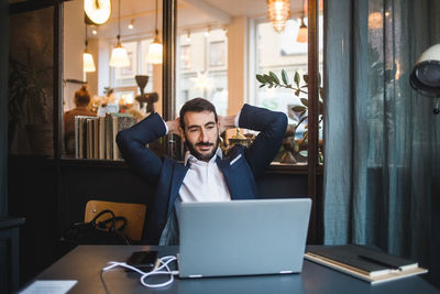 Businessman with hands behind head looking at laptop on desk in creative office