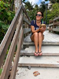 Woman having coconut water while sitting on steps at beach