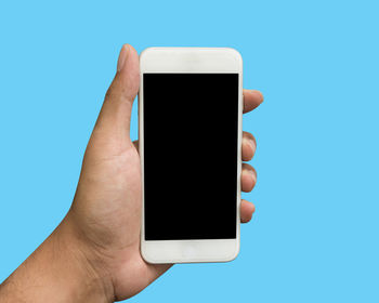 Cropped hand holding mobile phone against blue background