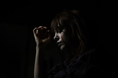 Close-up of young woman with halloween make-up against black background