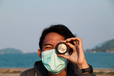 Portrait of man holding sunglasses against sea