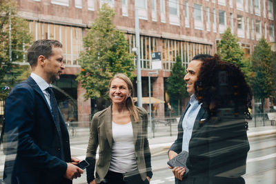 Smiling business colleagues discussing while standing on street seen from glass