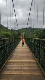 Woman walking on bridge against sky