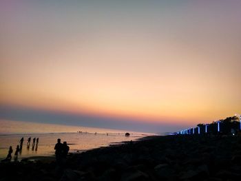 Silhouette people on beach against sky during sunset