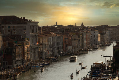 Boats in canal amidst buildings in city during sunset