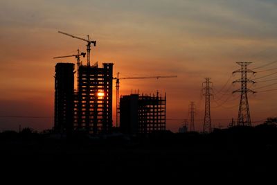 Silhouette cranes at construction site during sunset