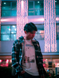 Full length of young man standing against illuminated light at night