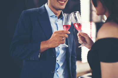 Midsection of happy couple toasting red wineglasses while standing in bar