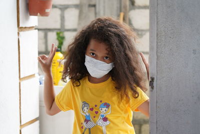 Portrait of smiling girl wearing ask standing by wall