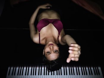 Portrait of young woman lying on grand piano against black background