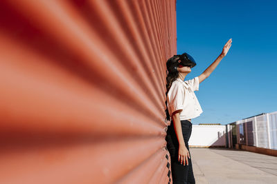 Young woman with virtual reality headset leaning on red wall