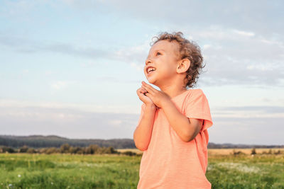 Girl looking away while standing on field against sky