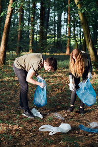 Young man and woman cleaning up a forest. volunteers picking plastic waste to bags