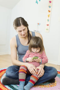 Pregnant woman looking at girl using mobile phone at home