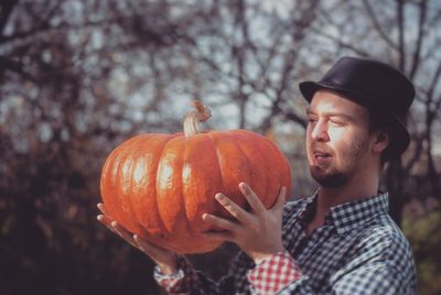 Young man holding pumpkin standing by tree outdoors