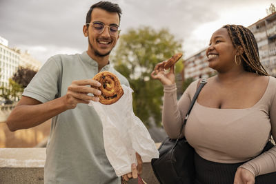 Happy man and woman with sweet food standing under sky