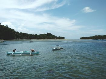 Men sitting in boat against sky at beach