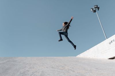 Low angle view of young woman jumping against clear sky