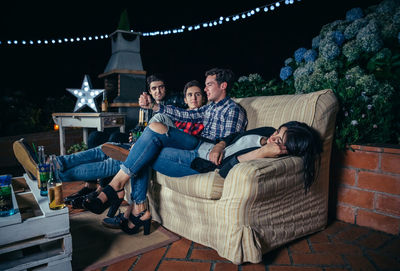 Woman sleeping with male friends talking on sofa at patio during night