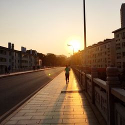 Woman walking on city against sky during sunset