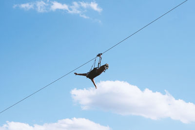 Low angle view of person hanging on rope against blue sky