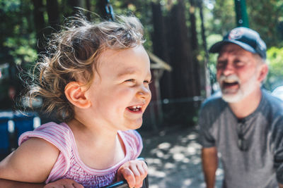 Cheerful granddaughter playing at playground by grandfather