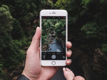 Cropped hand of man photographing river through smart phone