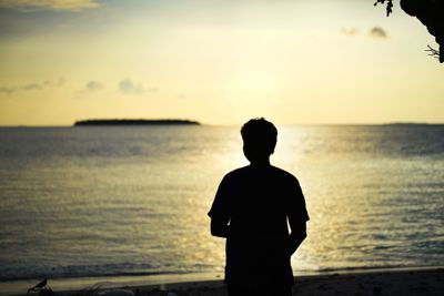 Rear view of silhouette man standing at beach during sunset