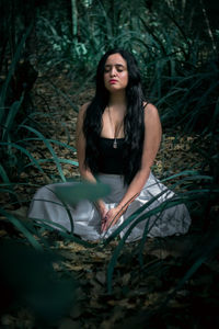 Woman with eyes closed mediating on land in forest