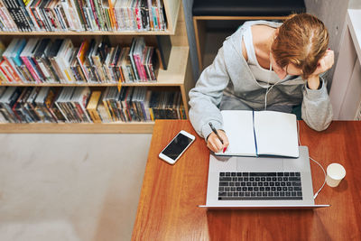 Student learning in university library. young woman reading textbook and making notes using computer