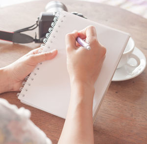 Cropped hands of woman writing on note pad at table