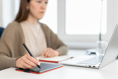 Selective focus on woman's hand with pencil for digital tablet. graphic designer working on laptop.