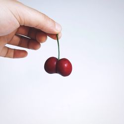 Close-up of hand holding strawberry over white background