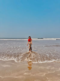 Rear view of woman standing at beach against clear sky