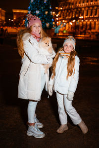 Lovely sisters teenagers walk on christmas eve along streets of evening city.