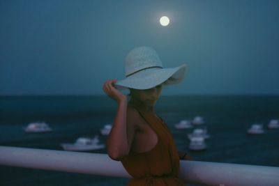 Woman wearing hat at beach against sky during dusk