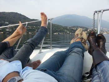 Low section of men sitting on riverbank against sky