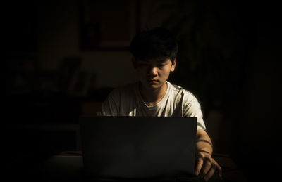 Portrait of teenage asian boy using laptop indoor with sunlight and shadow