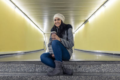 Young latina sitting on the subway steps with her coffee to go