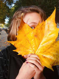 Low section of woman standing on yellow maple leaf during autumn