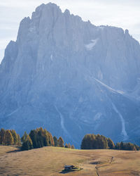 Small cottage in autumnal landscape with huge rock mountain in backdrop, vertical, dolomites